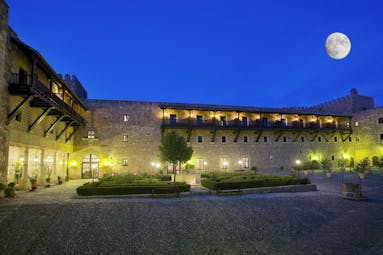 Exterior at night with hotel dimly lit up with wall lights and moon shining in the sky 