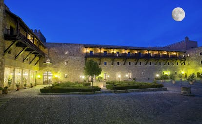 Exterior at night with hotel dimly lit up with wall lights and moon shining in the sky 
