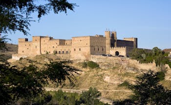 Exterior view of hotel with large castle like building in background on top of grassy mound 