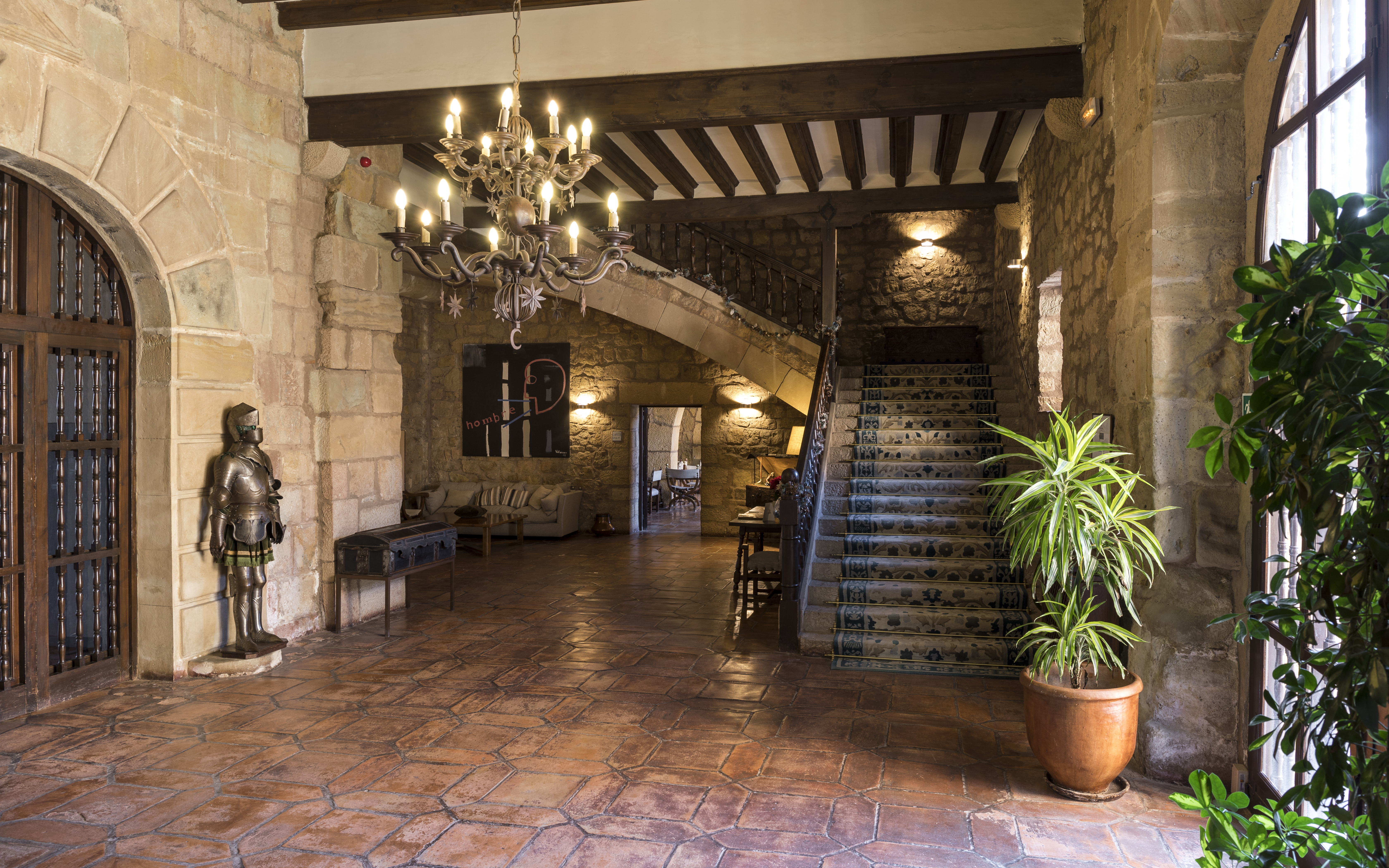 Lobby with chandelier in middle of room, stairs leading upstairs and statues and plants scattered around the room 
