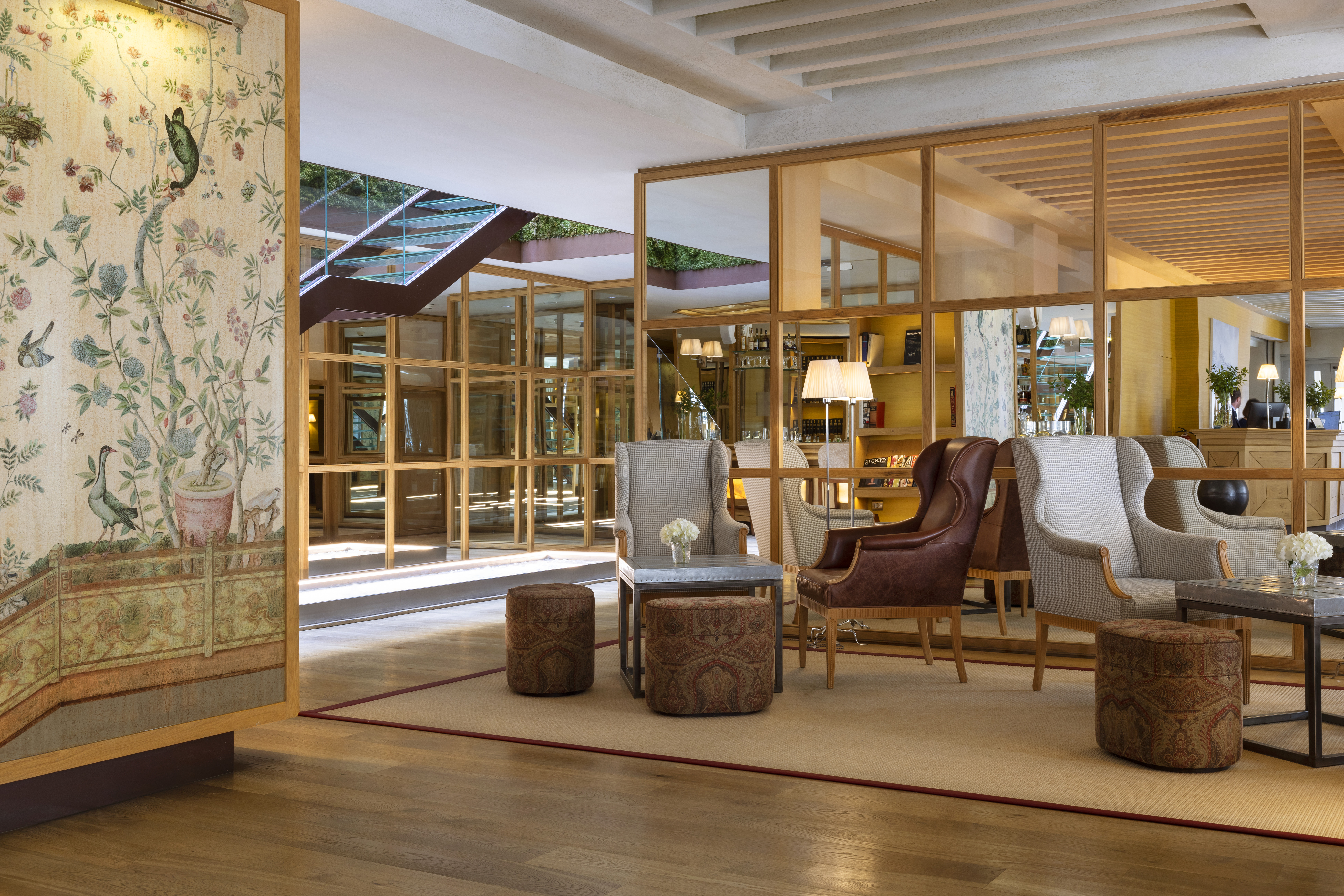 Hotel Urso grand lobby, with elegant armchairs, patterned wallpaper and modern glass dividers, with a warm wooden decor style