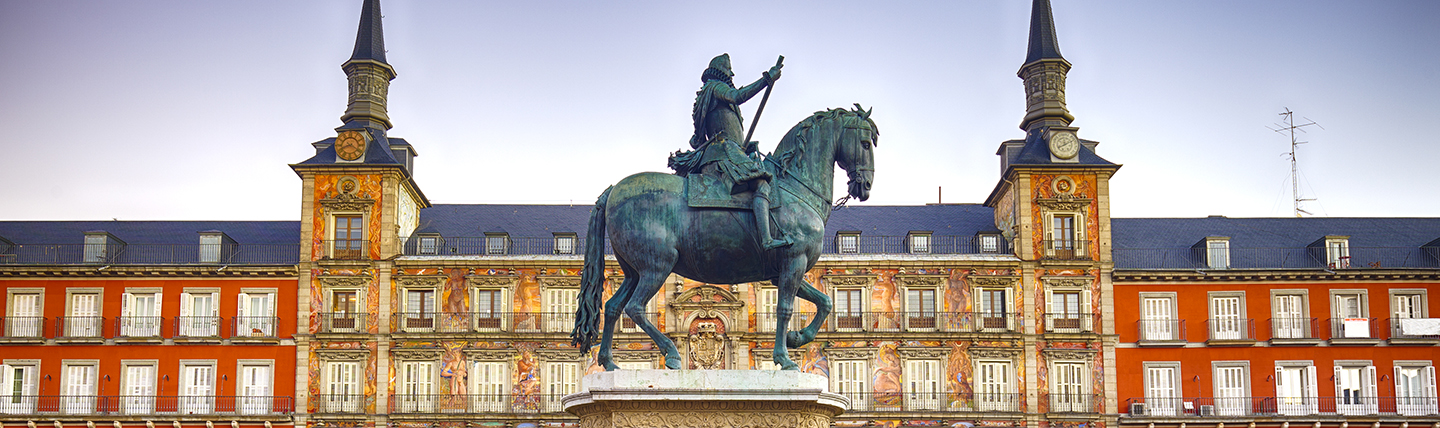 Man on statue in front of orange coloured palatial buildings in Madrid