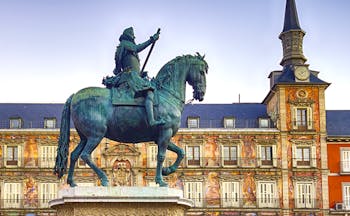 Man on statue in front of orange coloured palatial buildings in Madrid