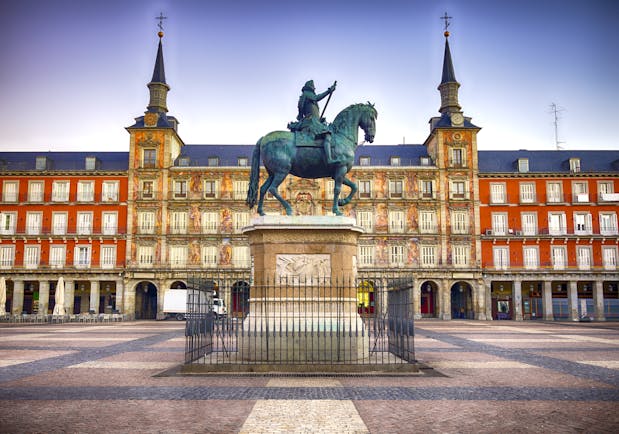 Equestrian statue in bronze with orange facade to buildings lining the arcaded square of the Plaza Mayor in Madrid