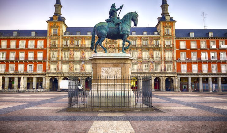 Equestrian statue in bronze with orange facade to buildings lining the arcaded square of the Plaza Mayor in Madrid