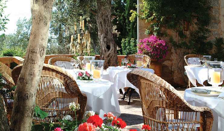 Belmond la Residencia Mallorca terrace restaurant outdoor dining area with wicker chairs candelabra and flowers