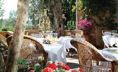 Belmond la Residencia Mallorca terrace restaurant outdoor dining area with wicker chairs candelabra and flowers