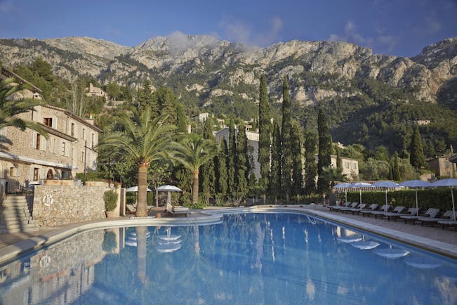 La Residencia Mallorca outdoor swimming pool loungers umbrellas palm trees next to stone building mountain view