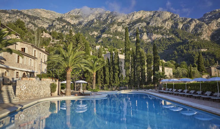 La Residencia Mallorca outdoor swimming pool loungers umbrellas palm trees next to stone building mountain view