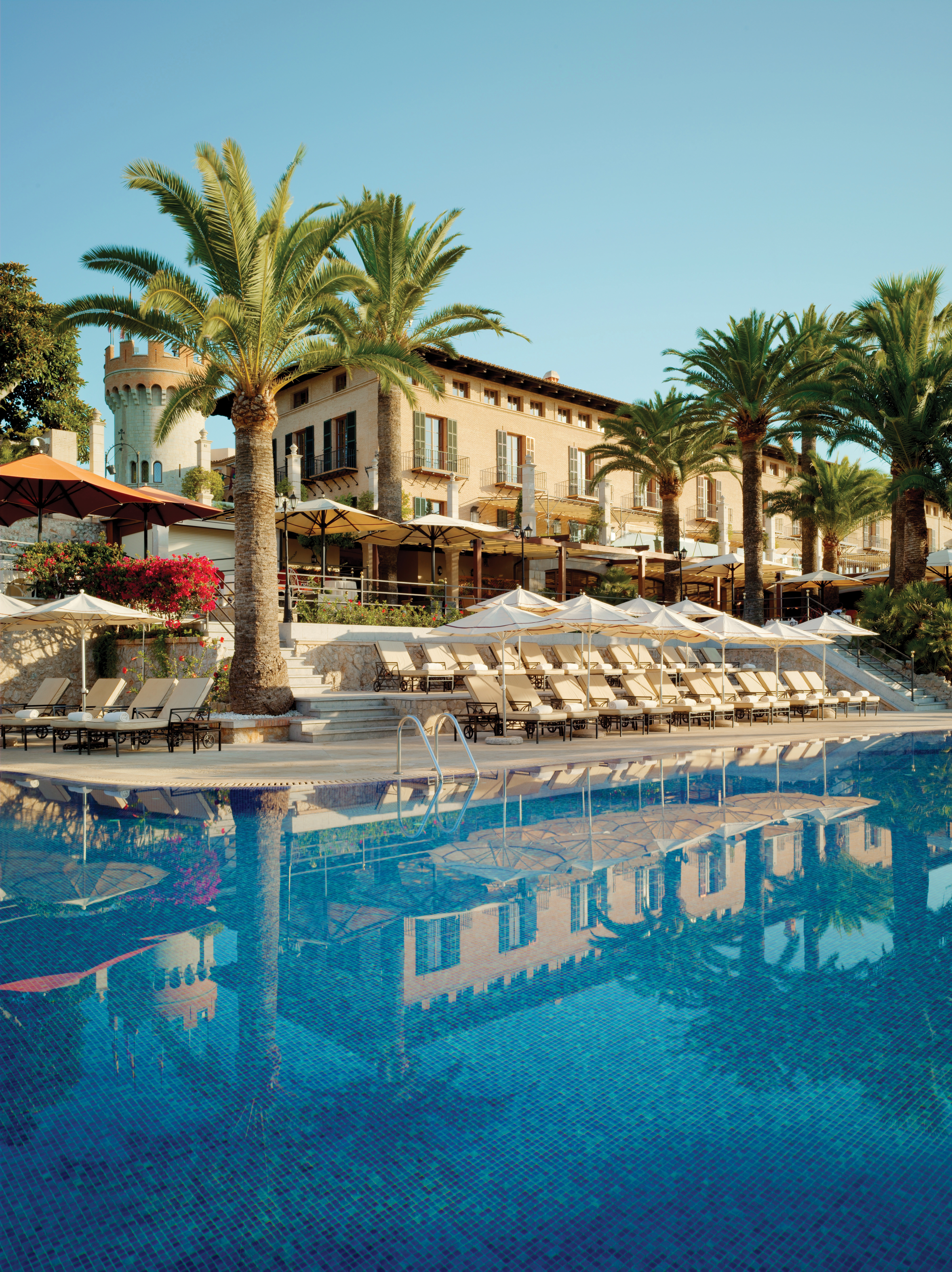 Outdoor pool with sun loungers, palm trees and hotel building behind