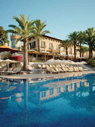 Outdoor pool with sun loungers, palm trees and hotel building behind