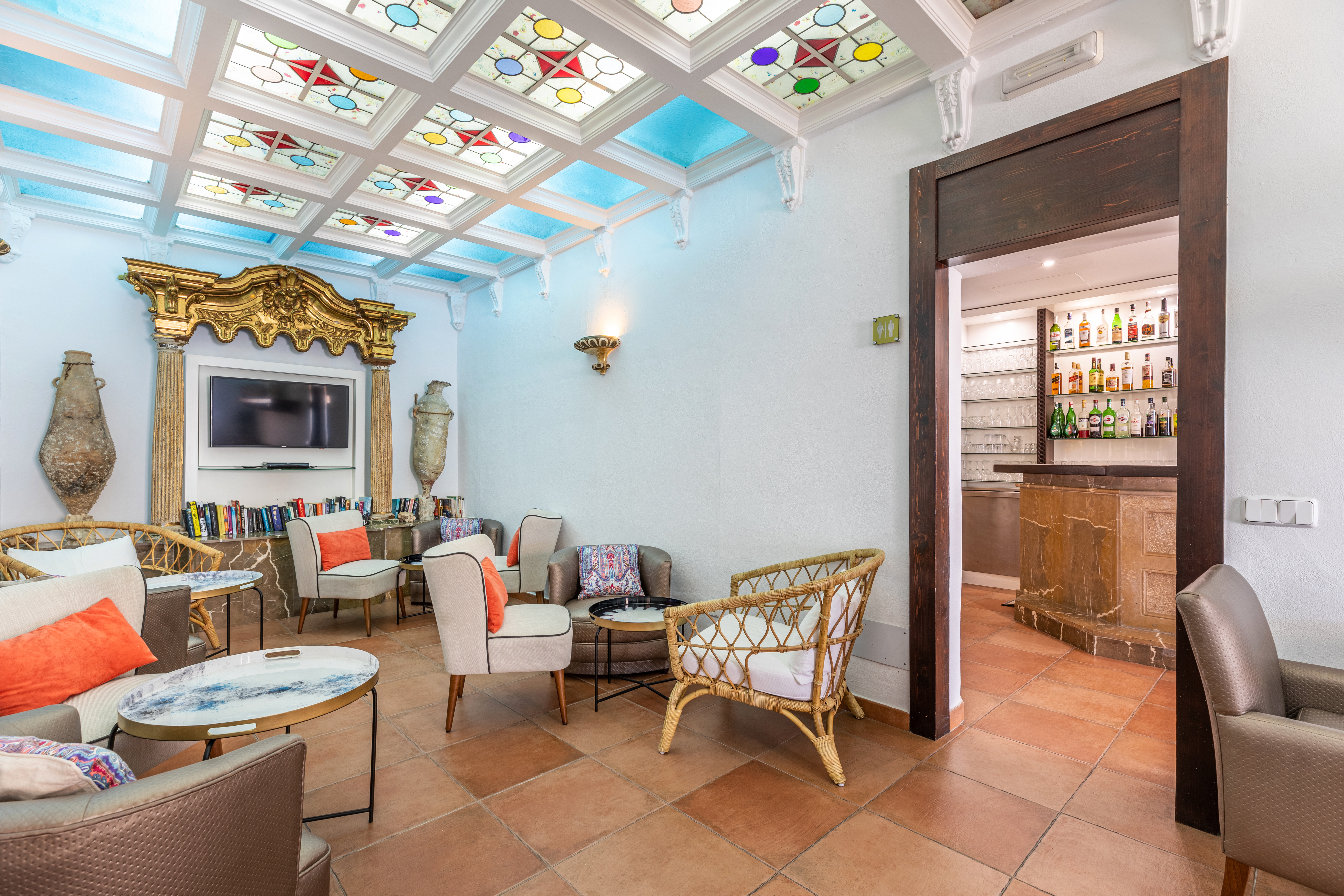Hotel Hoposa Bahia bar, with ornate details on the walls, mismatched armchairs, and colourful stained glass ceiling