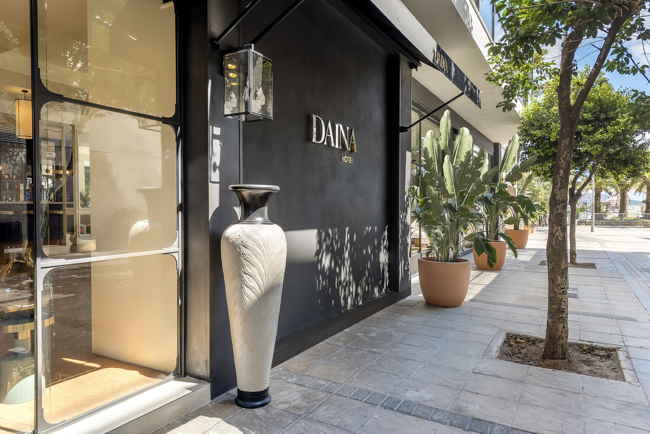 Hotel Hoposa Daina front entrance, with black modern walls, terracotta pots of palms, glass doors, and tall vases