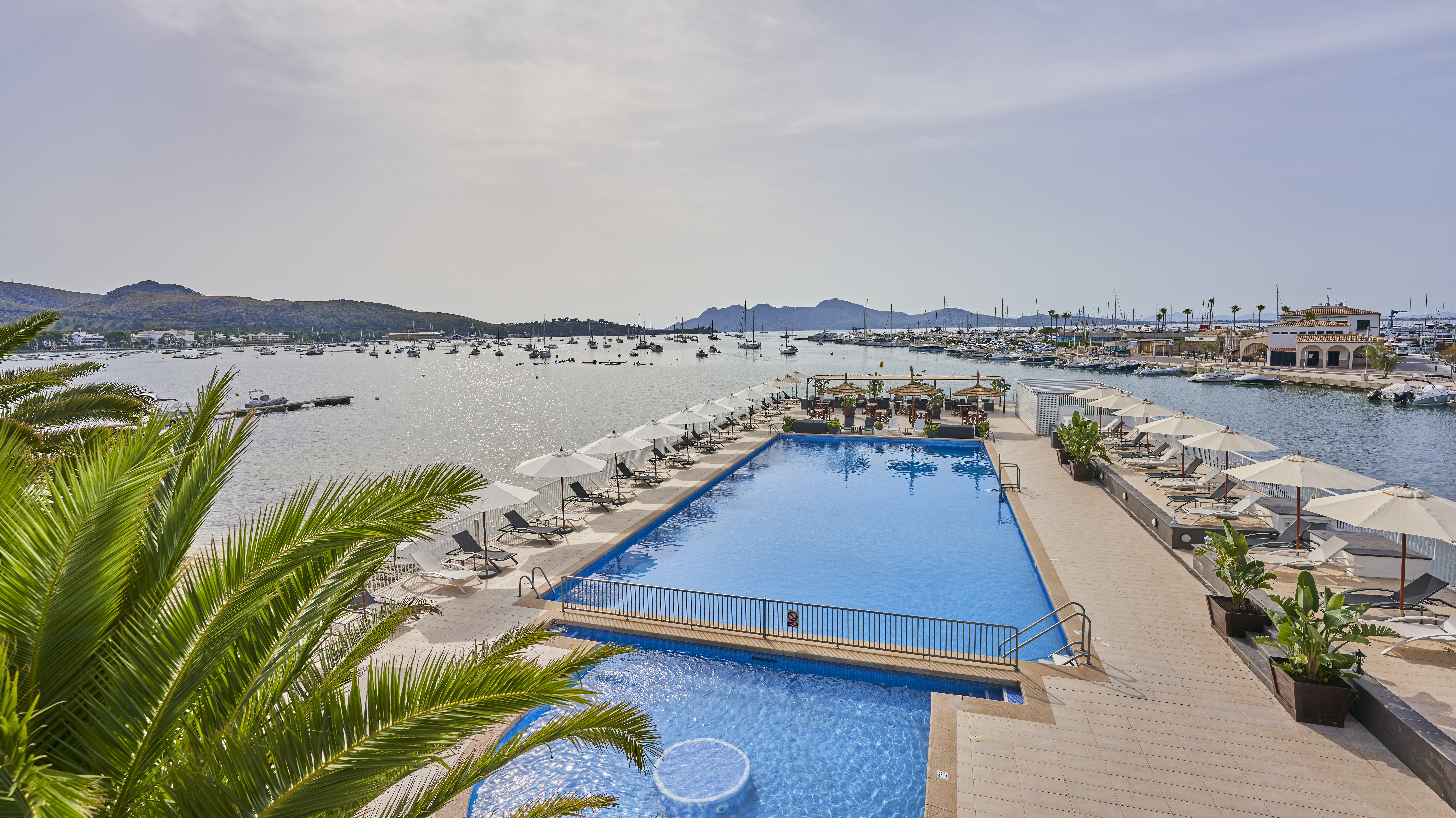 Hotel Hoposa Daina poolside, looking out from the hotel across the pool and the sun loungers towards the sea and the marina