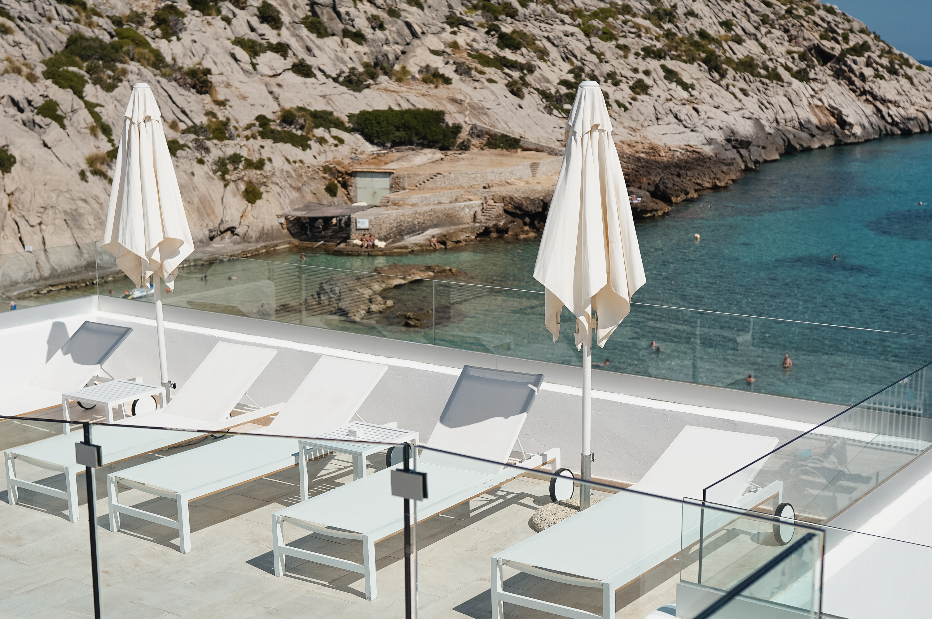 Hotel Hoposa Niu view down to the beach from the poolside, with clear waters and rocky cliffside