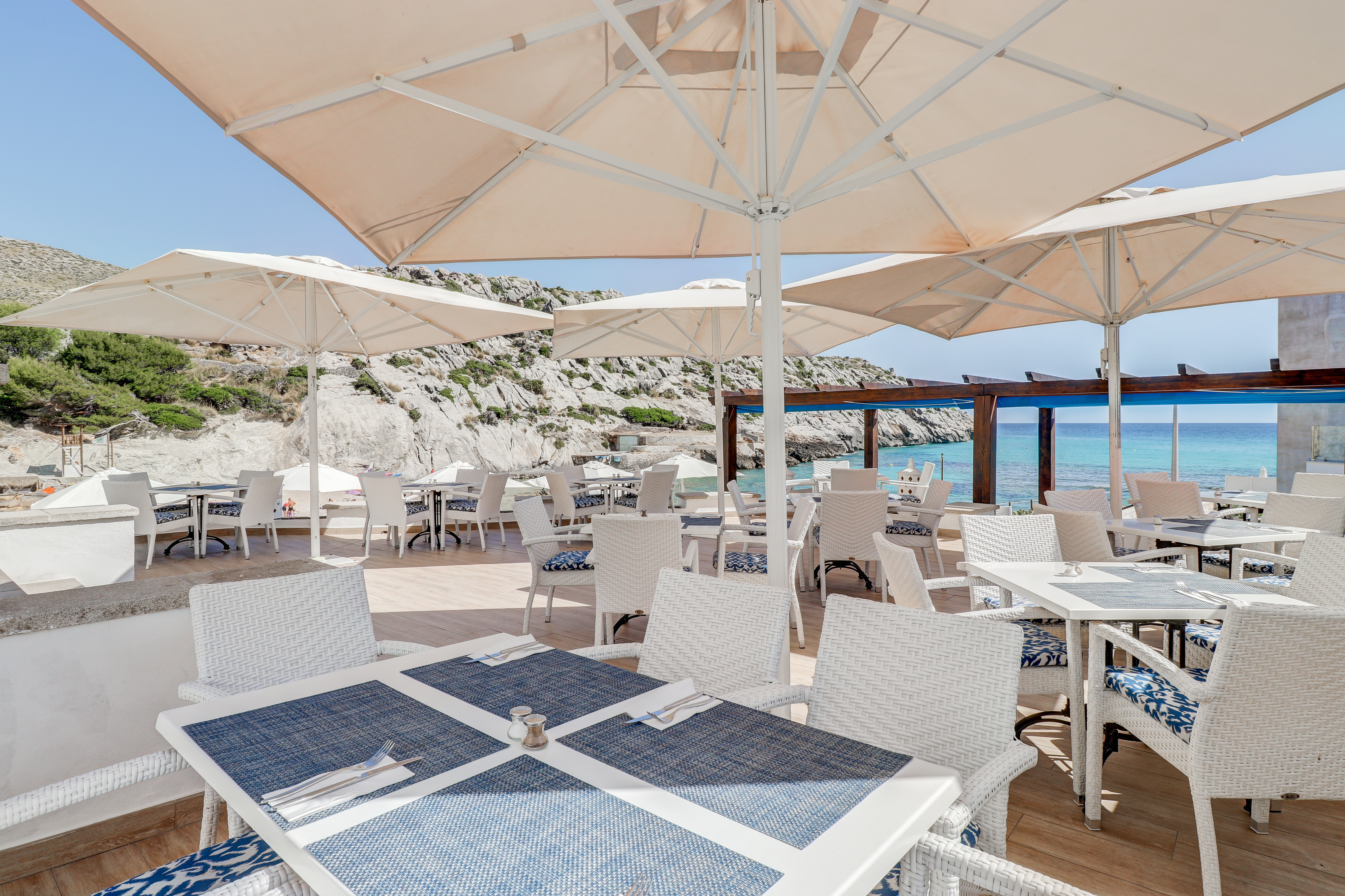 Hotel Hoposa Niu restaurant dining on the terrace, with white tables, chairs, and parasols, and the sea in the distance