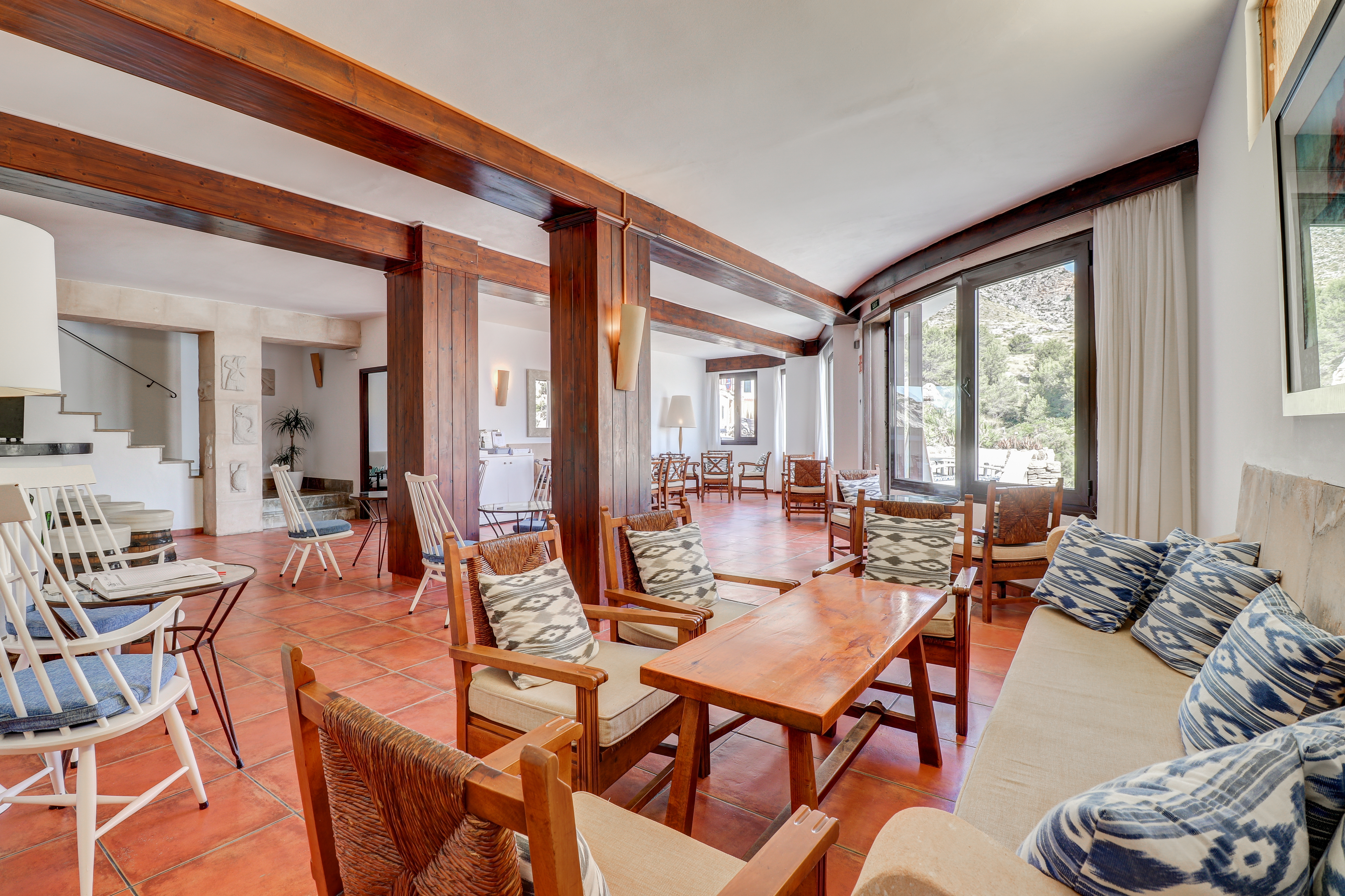 Hotel Hoposa Niu characterful interior with terracotta tiles, dark wooden beams, and patterned blue cushions on white and brown chairs