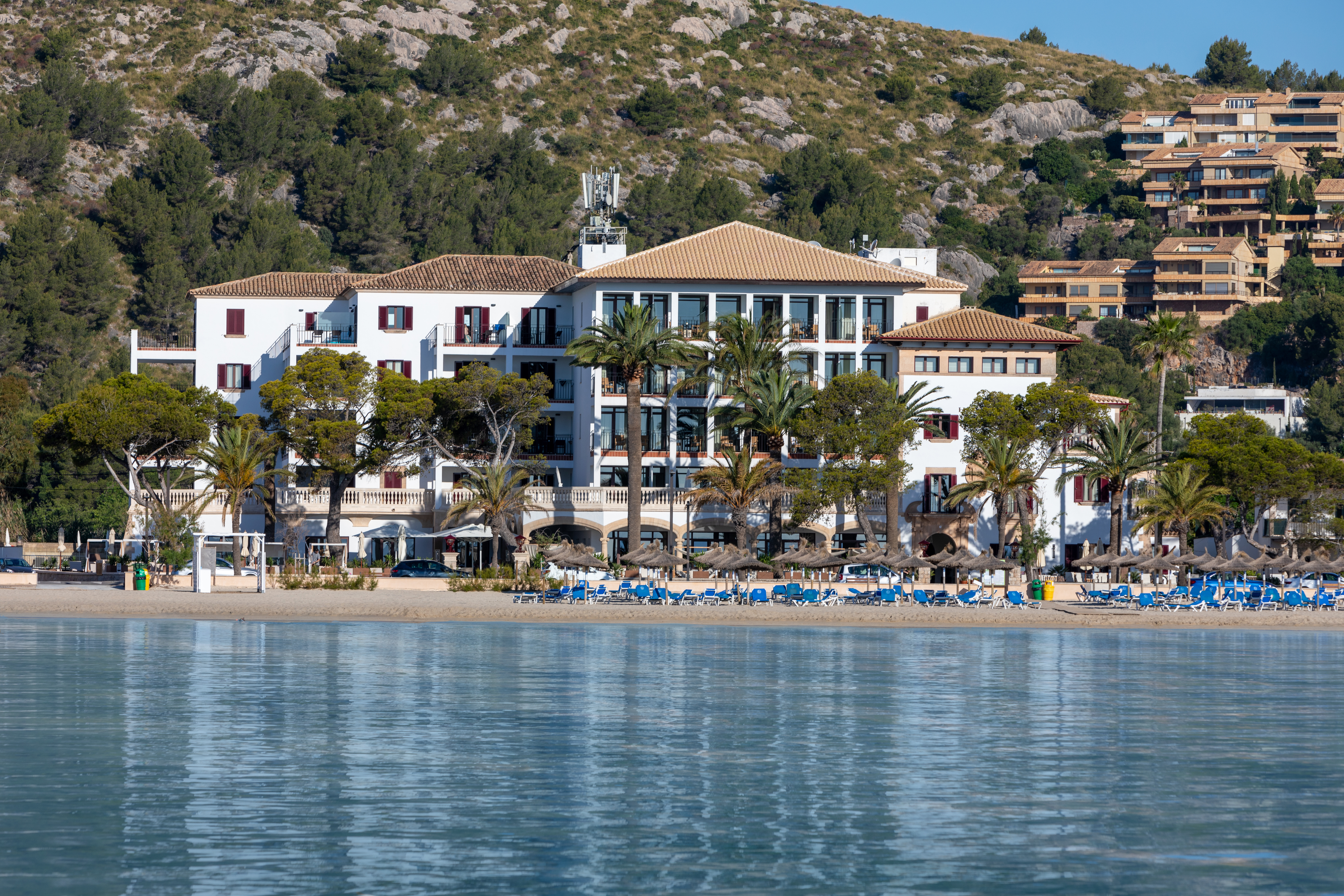 Hotel Hoposa Uyal hotel building, as seen from sea looking back towards the shore, with Aleppo pine trees and hills in the distance