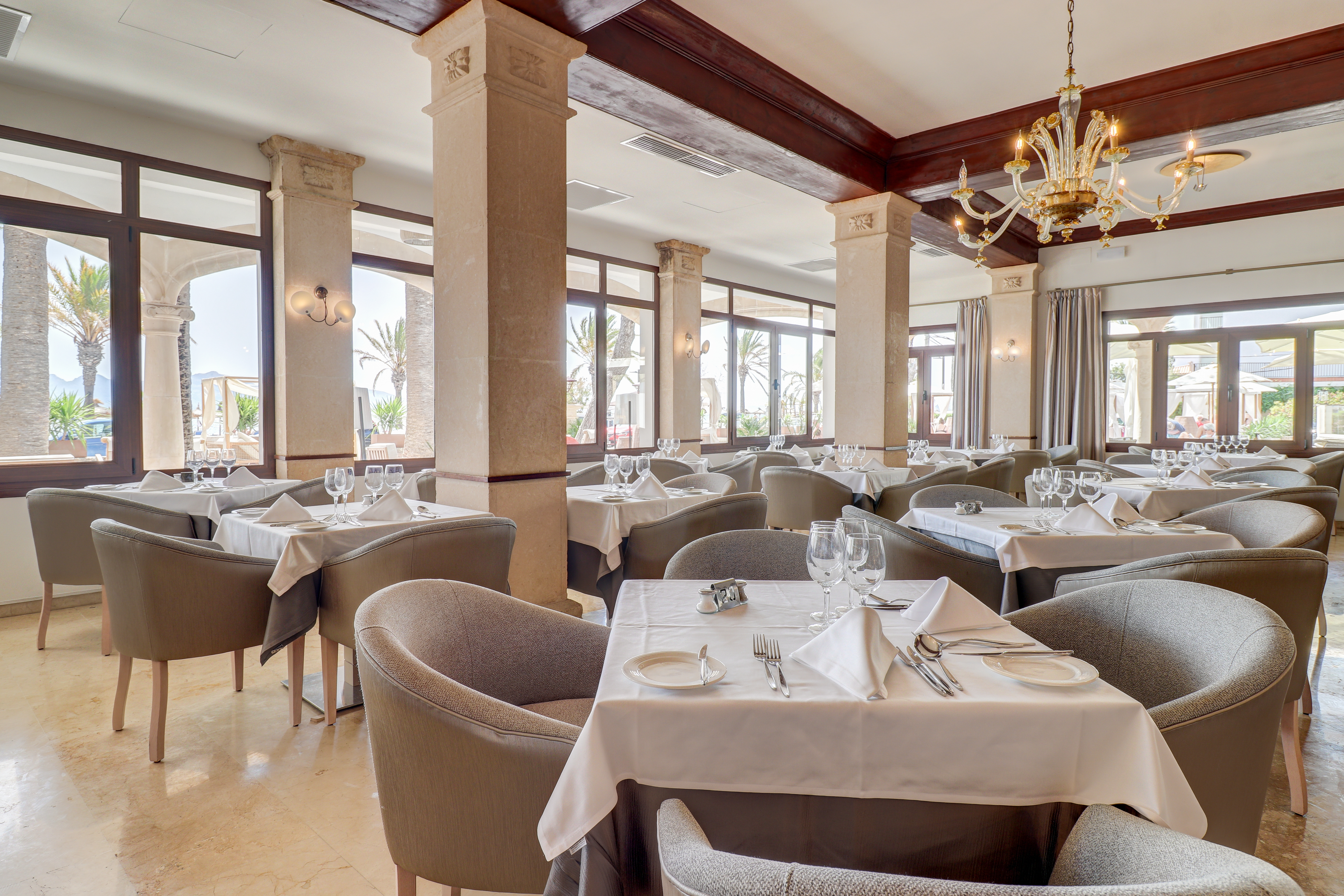 Hotel Hoposa Uyal restaurant with interior columns, comfortable armchairs around white-clothed tables, and floor-to-ceiling windows