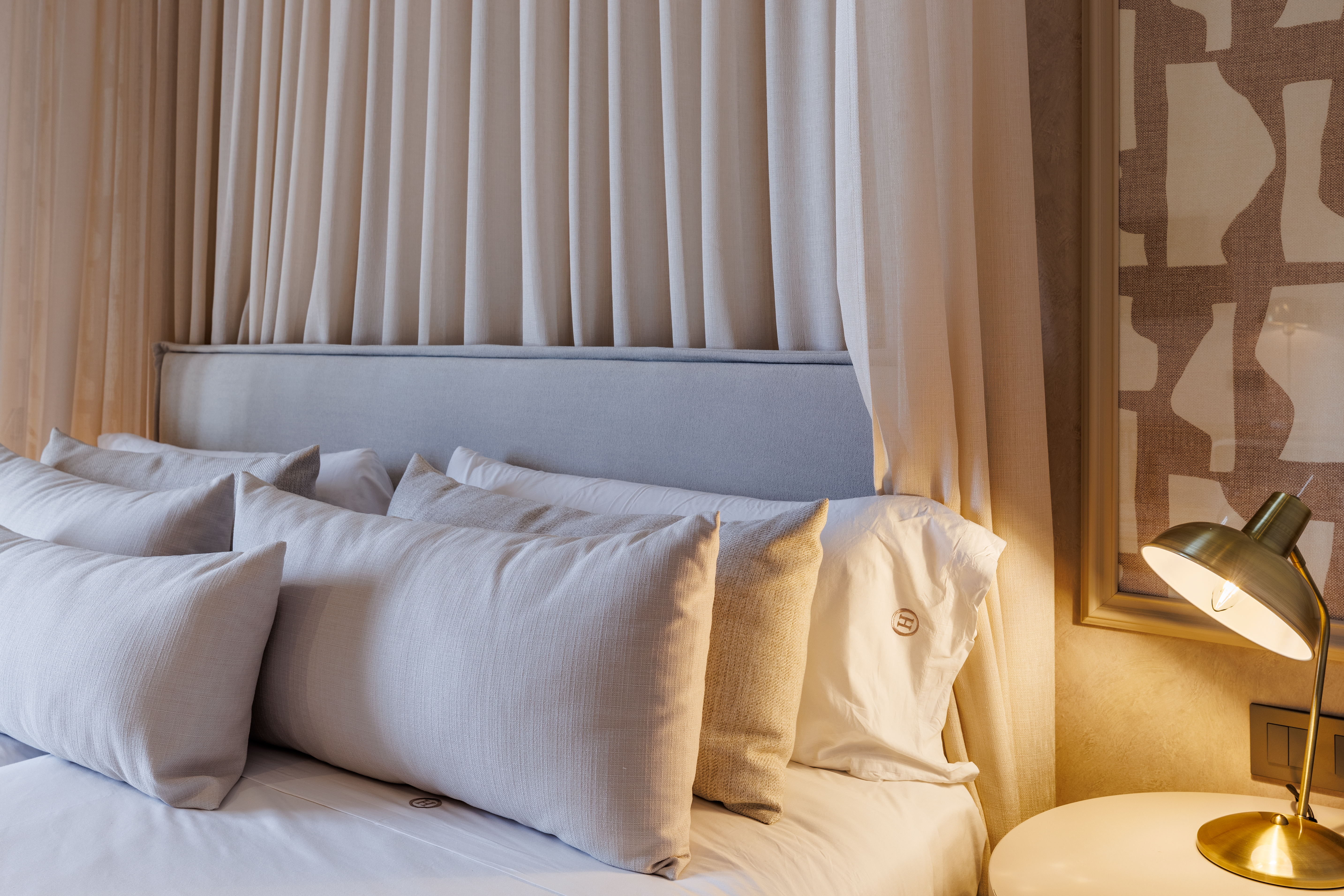Hotel Hoposa Uyal Standard room, close up of the bed, with plump pillows, hanging drapes behind the headboard, and beside lamp