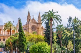 The spires and front of the Cathedral of Le Seu flanked by palm trees in Palma Mallorca