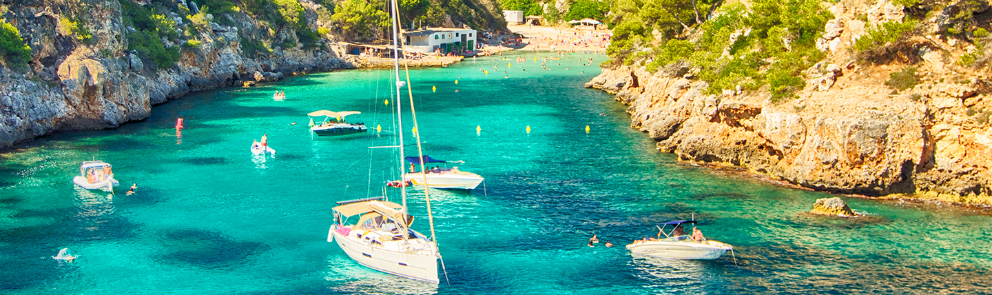 Small cove with wooded cliffs and moored boats in bright green-blue water