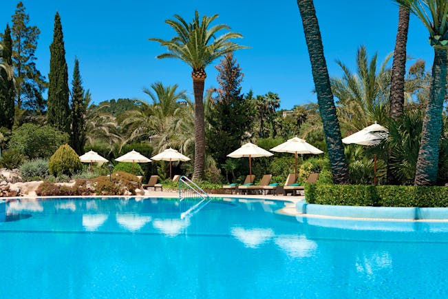 Swimming pool with white umbrellas and palm trees around the edges