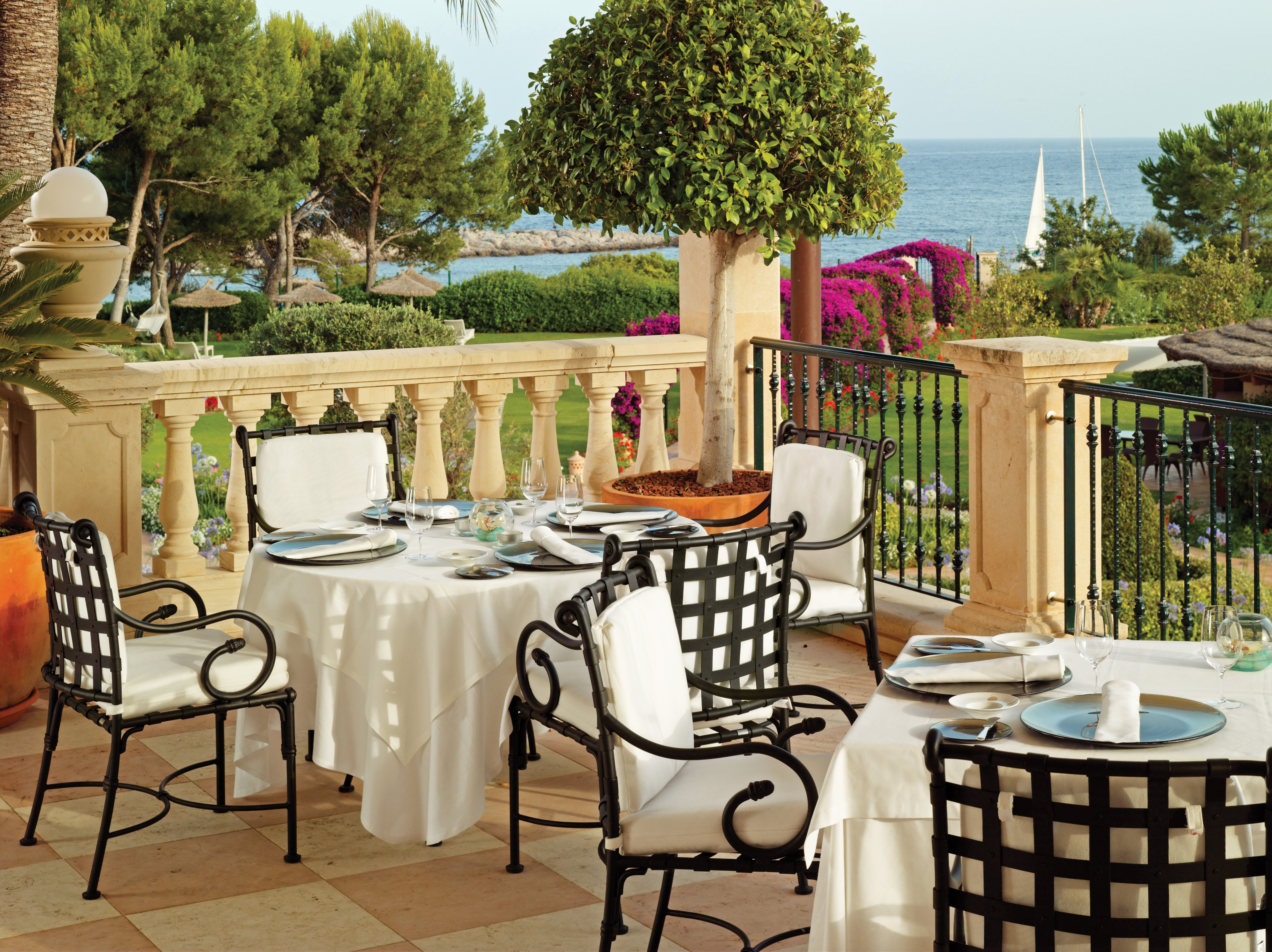 Outdoor dining terrace with tables and chairs set out overlooking trees and the sea
