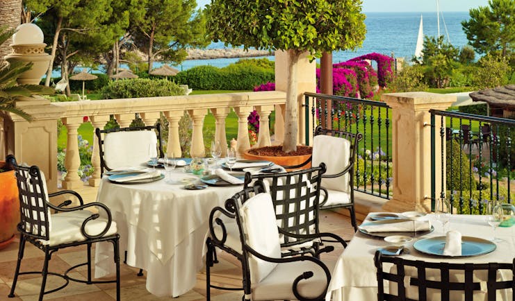 Outdoor dining terrace with tables and chairs set out overlooking trees and the sea