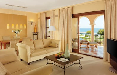 Ocean suite living space with cream colour scheme and bi-folding doors opening up onto a terrace balcony overlooking the sea