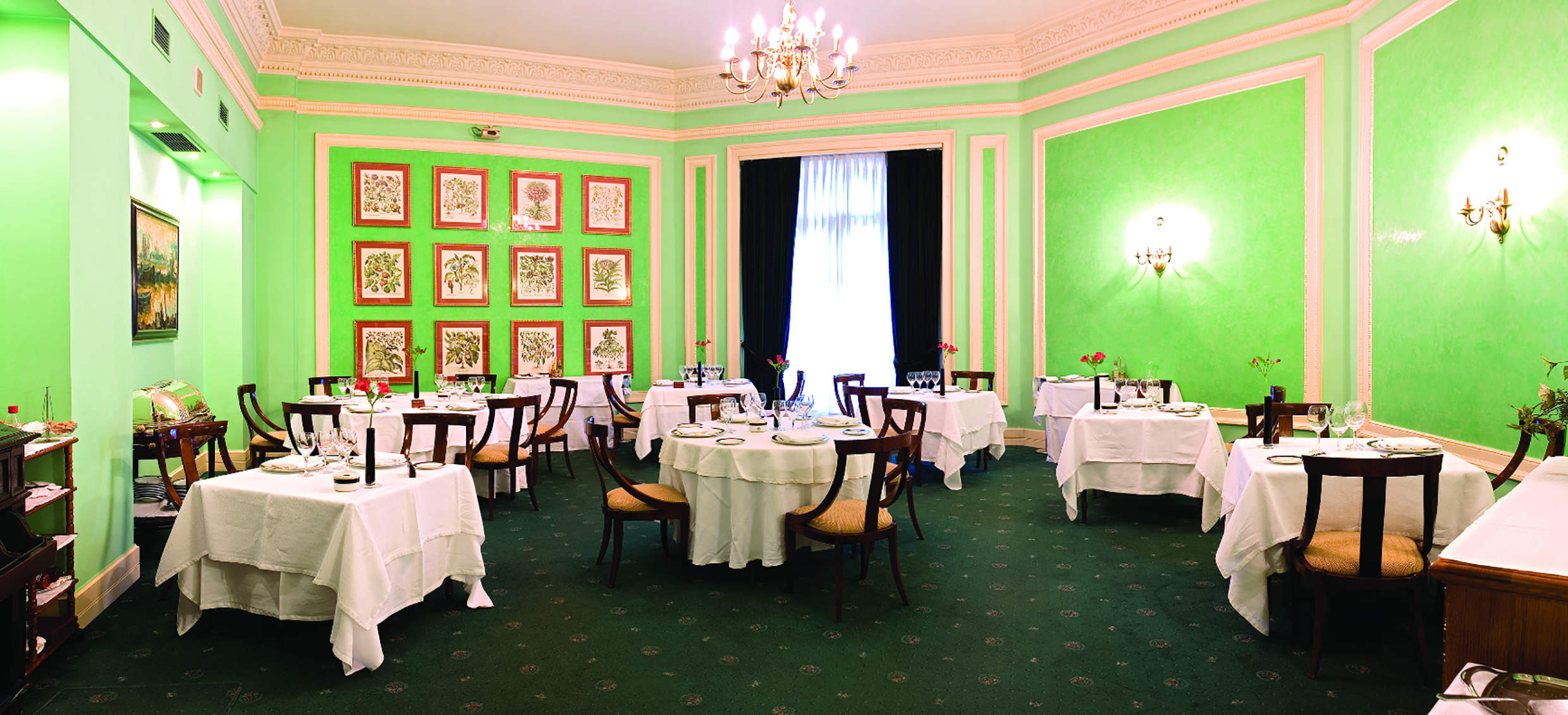 Restaurant with green walls, chandeliers and tables set out 
