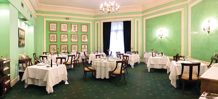Restaurant with green walls, chandeliers and tables set out 