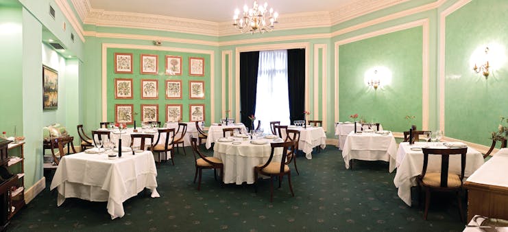 Restaurant with green walls, chandeliers and tables set out 