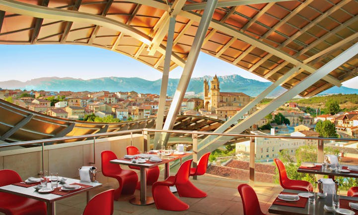 Outdoor restaurant dining area with wooden porch overhead, looking out over views of the city