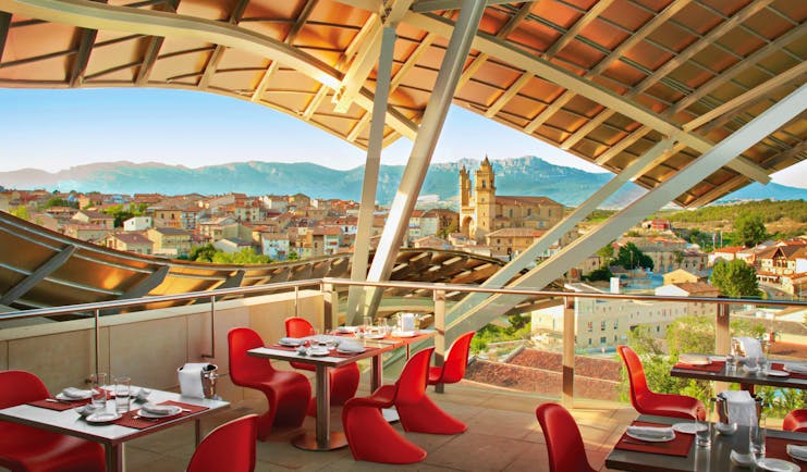Outdoor restaurant dining area with wooden porch overhead, looking out over views of the city