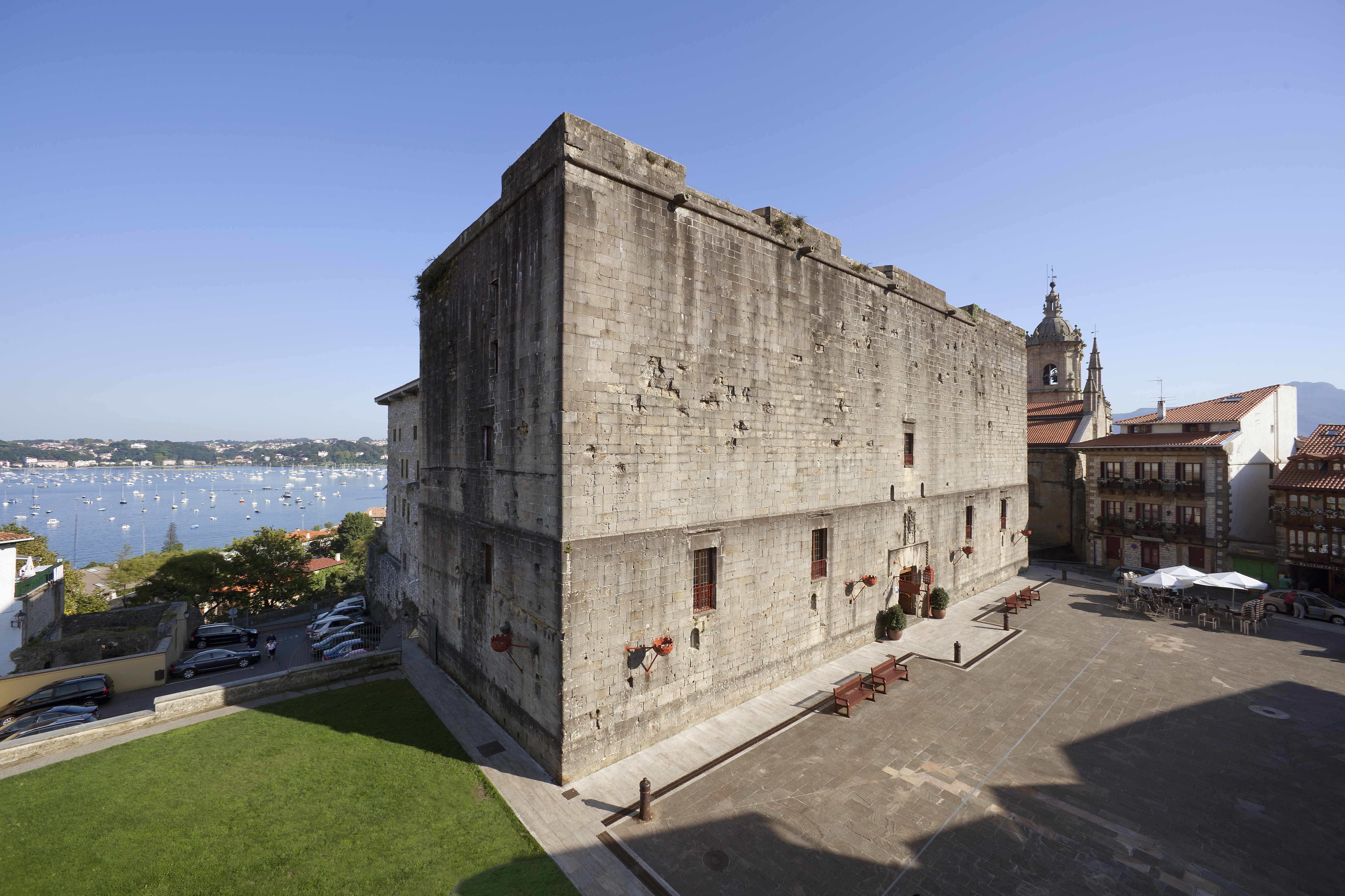 Exterior of hotel, a large stone building, grassy lawn beside it and ocean in the distance 