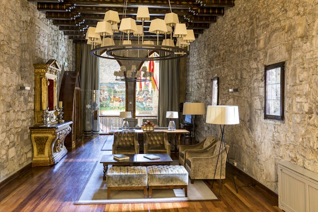 Lounge with stone walls, a large chandelier, sofas and arm chairs set out for sitting and art work on the walls