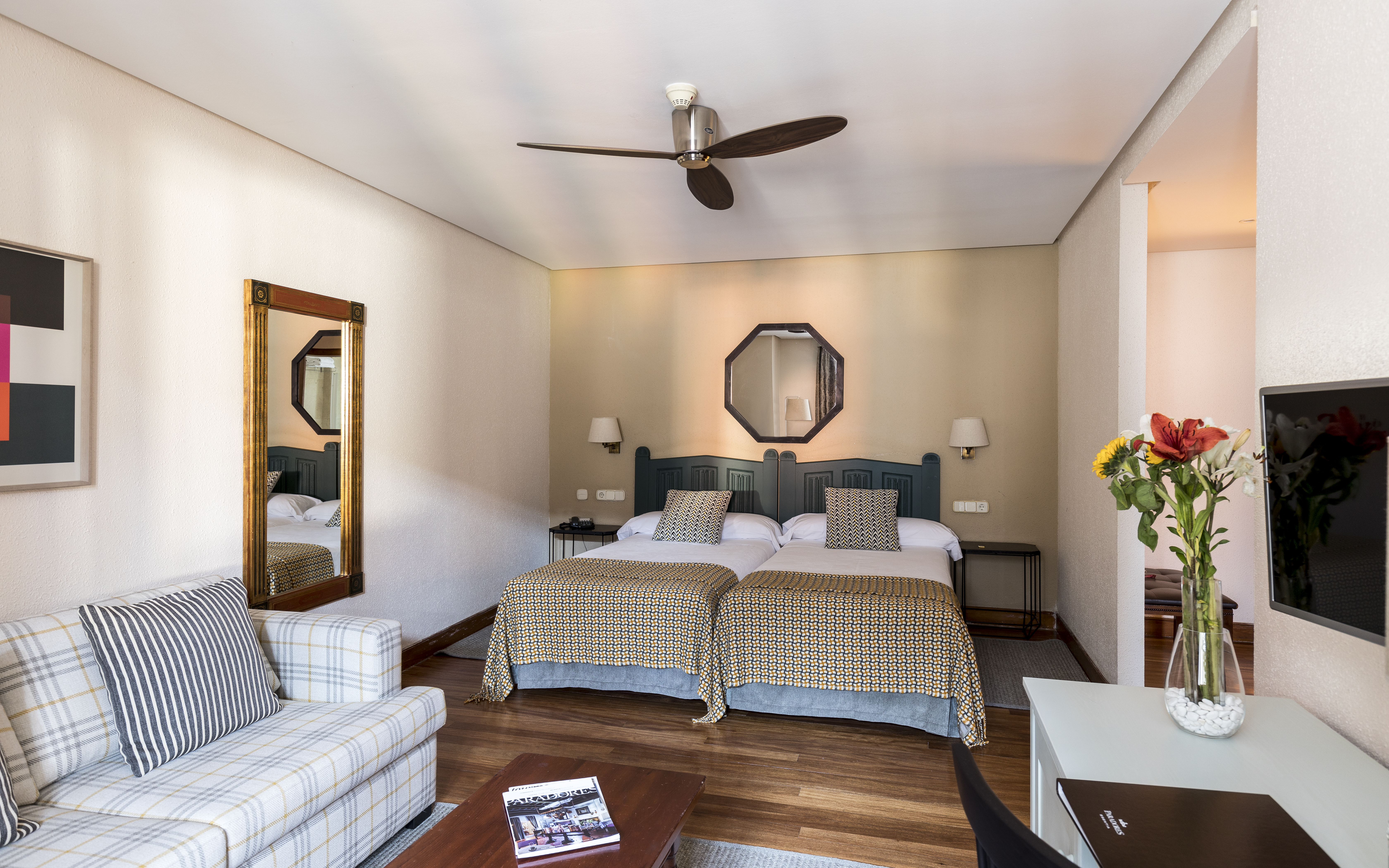 Bedroom with two twin beds joined as a double, a sofa, television, flowers and electric fan 