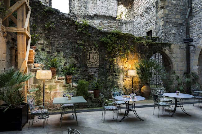 Outdoor terrace area with tables and chairs, lamps lighting up the stone walls and vines growing up them 