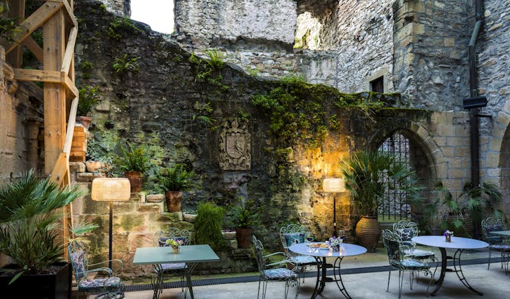 Outdoor terrace area with tables and chairs, lamps lighting up the stone walls and vines growing up them 