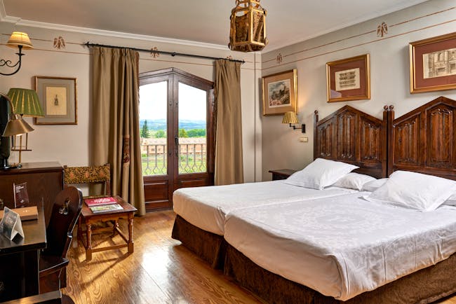 Standard double room with two double beds laid side by side, wooden doors opening onto a balcony with views over fields 