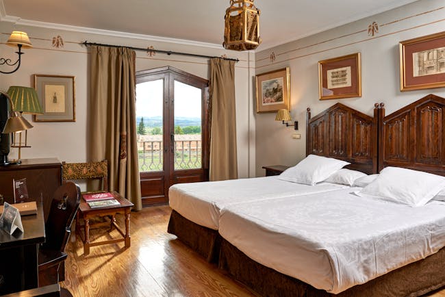 Standard double room with two double beds laid side by side, wooden doors opening onto a balcony with views over fields 