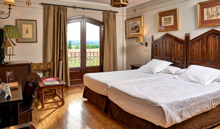 Standard double room with two double beds laid side by side, wooden doors opening onto a balcony with views over fields 