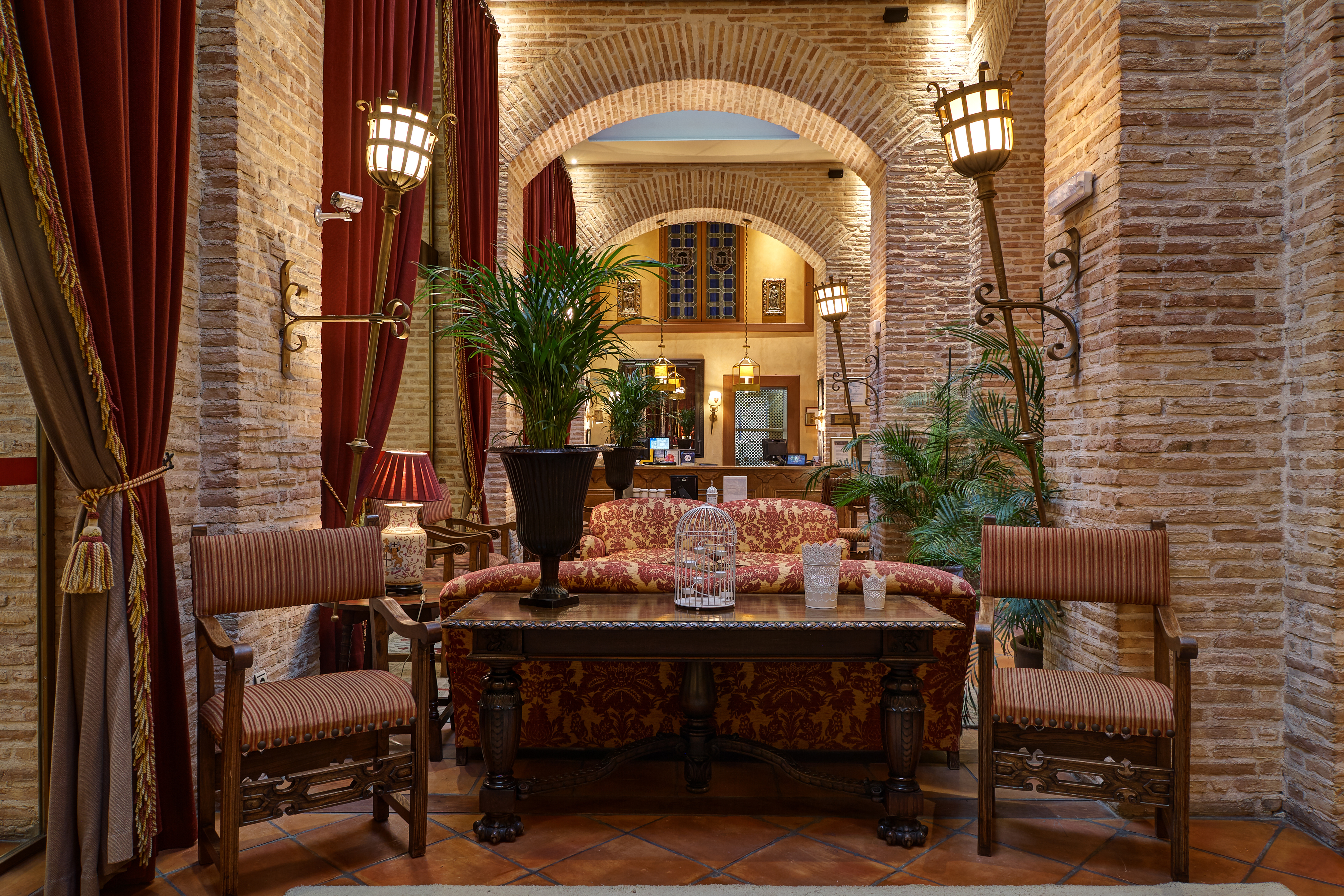 Reception with high ceilings and archways, arm chairs and sofas laid out for seating and potted plants scattered around the room 