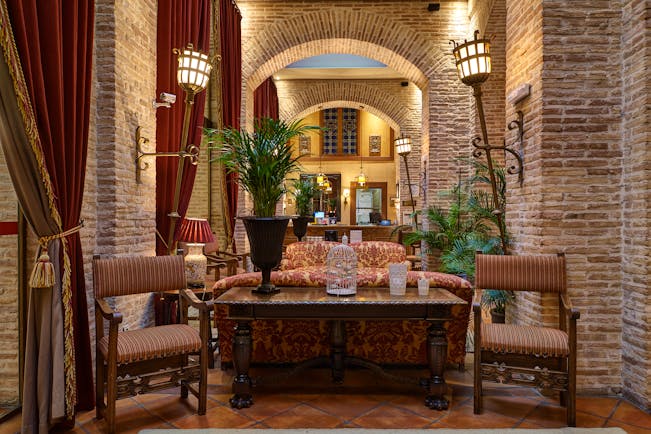 Reception with high ceilings and archways, arm chairs and sofas laid out for seating and potted plants scattered around the room 
