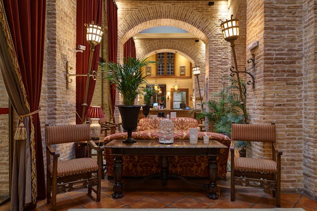 Reception with high ceilings and archways, arm chairs and sofas laid out for seating and potted plants scattered around the room 