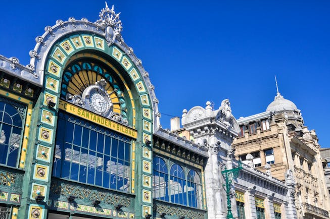 Ornate and elaborate facade with glass panels and green and yellow tiles of the Abando railway station in Bilbao