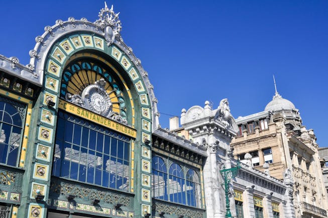 Ornate and elaborate facade with glass panels and green and yellow tiles of the Abando railway station in Bilbao