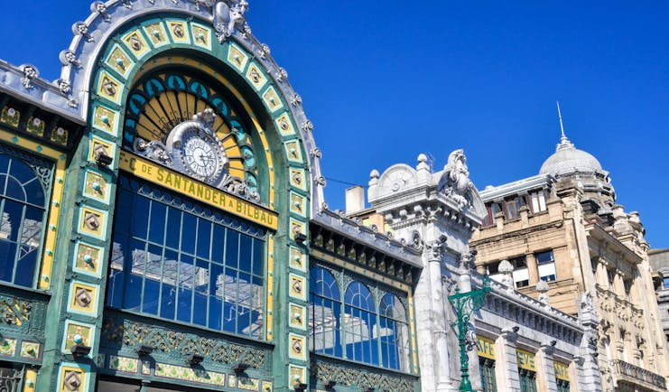 Ornate and elaborate facade with glass panels and green and yellow tiles of the Abando railway station in Bilbao