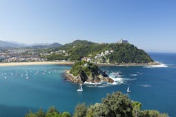 Sailing boats on blue sea in front of small island in bay with yellow sand beach in background at San Sebastian